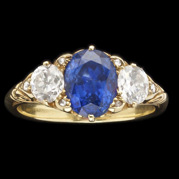 Edwardian sapphire and diamond ring, the sapphire 2.67cts, 2 side diamonds= 0.96cts, G-H colour, in a carved scrolled 18ct yellow gold setting